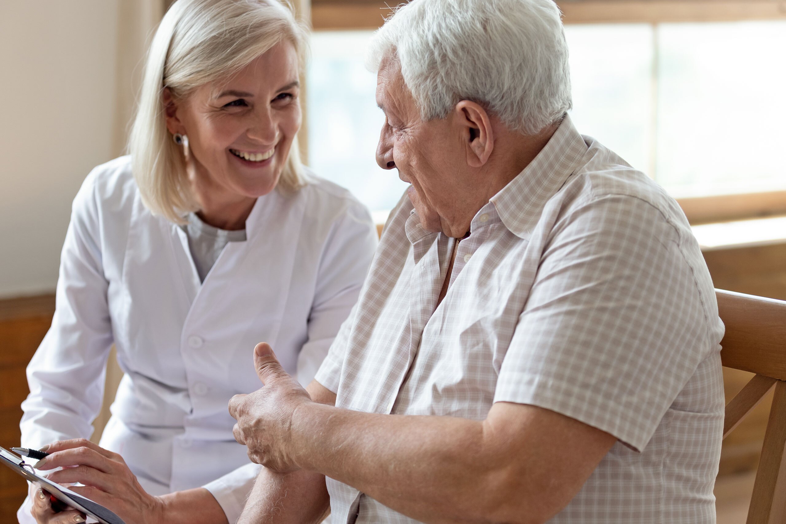 Elderly man and therapist holding clipboard writing personal information having pleasant warm conversation.