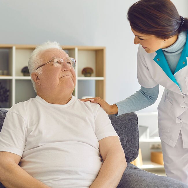 A seated resident looks up at a comforting team member.