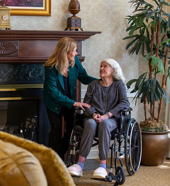 A resident sits in a wheelchair talking to another lady in green.