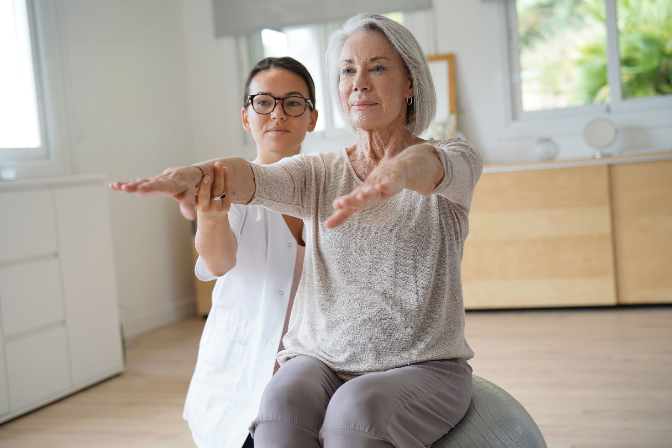 Senior woman exercising with her physiotherapist and swiss ball.