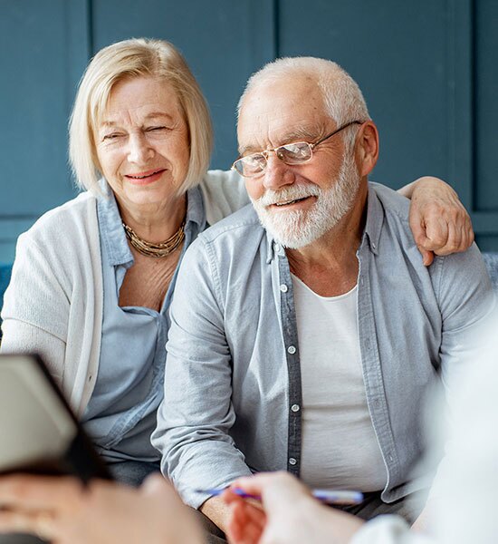 A couple smiling while talking to somebody going over documents.