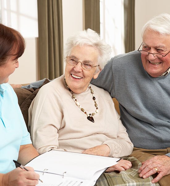 A couple smiling while talking to somebody with a binder going over documents.