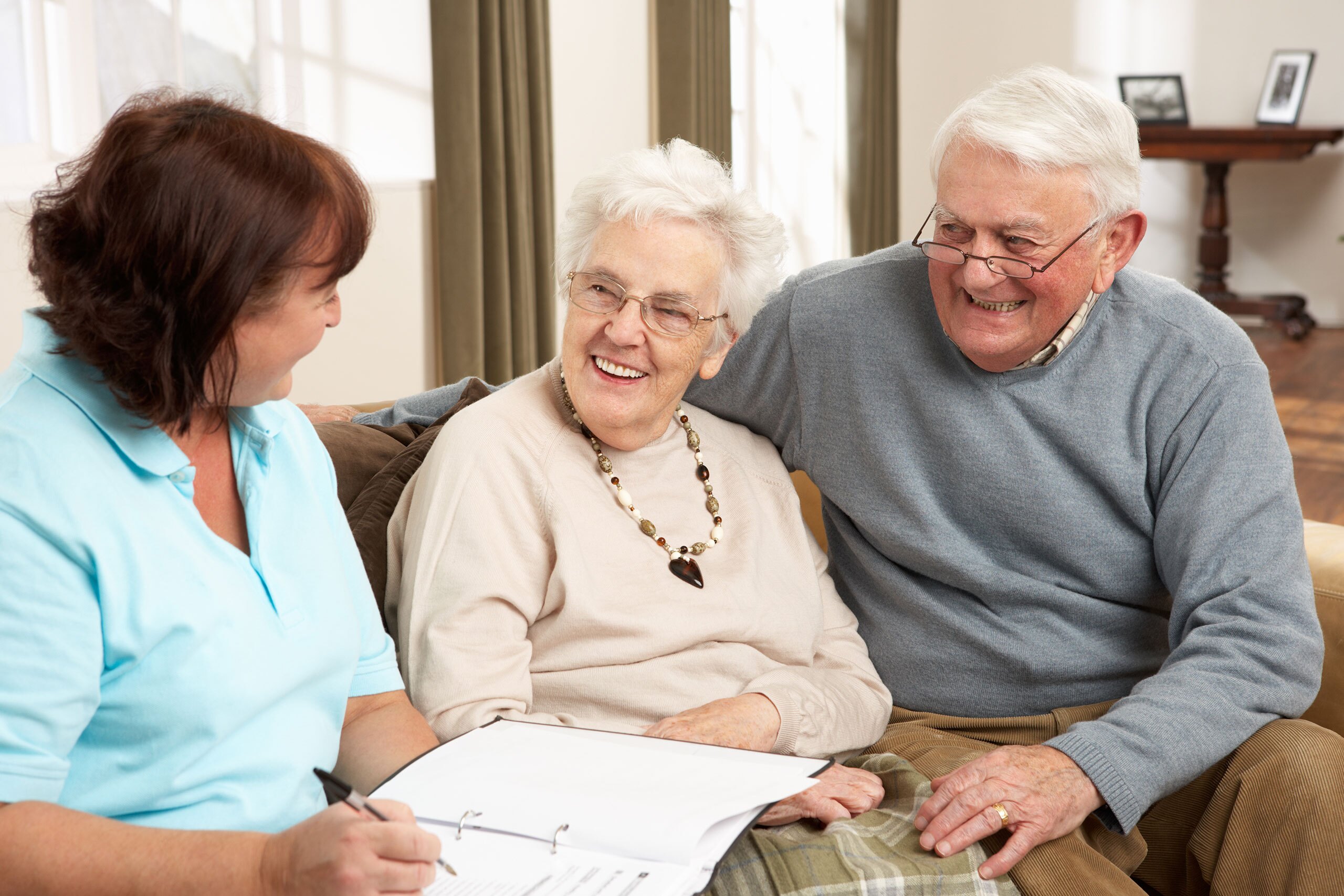A couple smiling while talking to somebody with a binder going over documents.