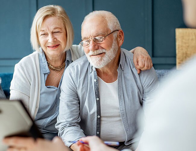 A couple smiling while talking to somebody going over documents.