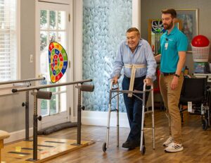 A resident is supported by a therapy staff member while walking with a walker.