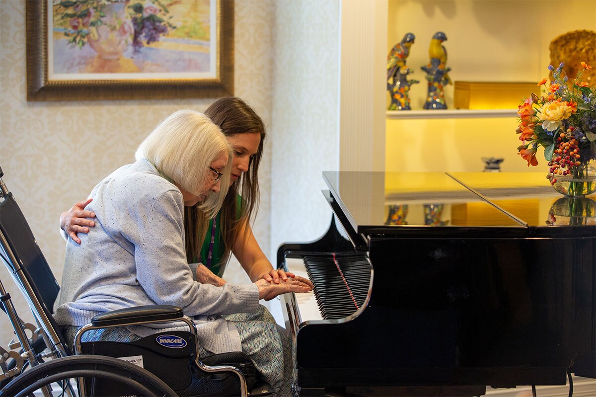 A resident in a wheelchair plays the piano with assistance.