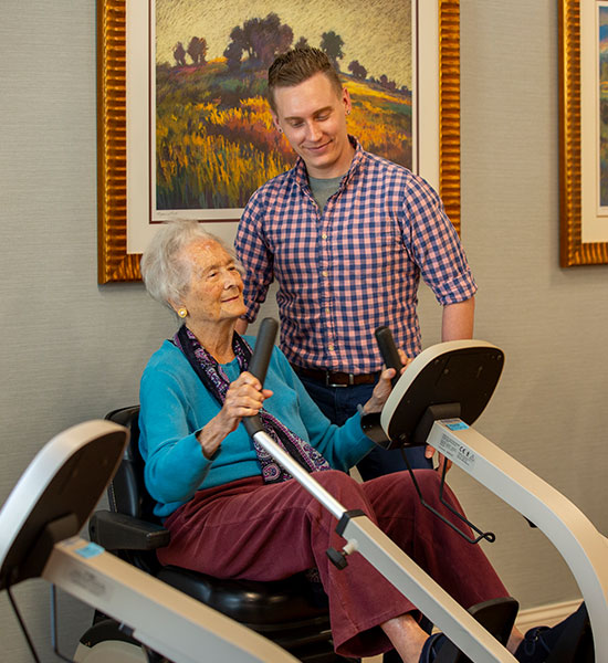 A resident sits on some exercise equipment while somebody monitors things.